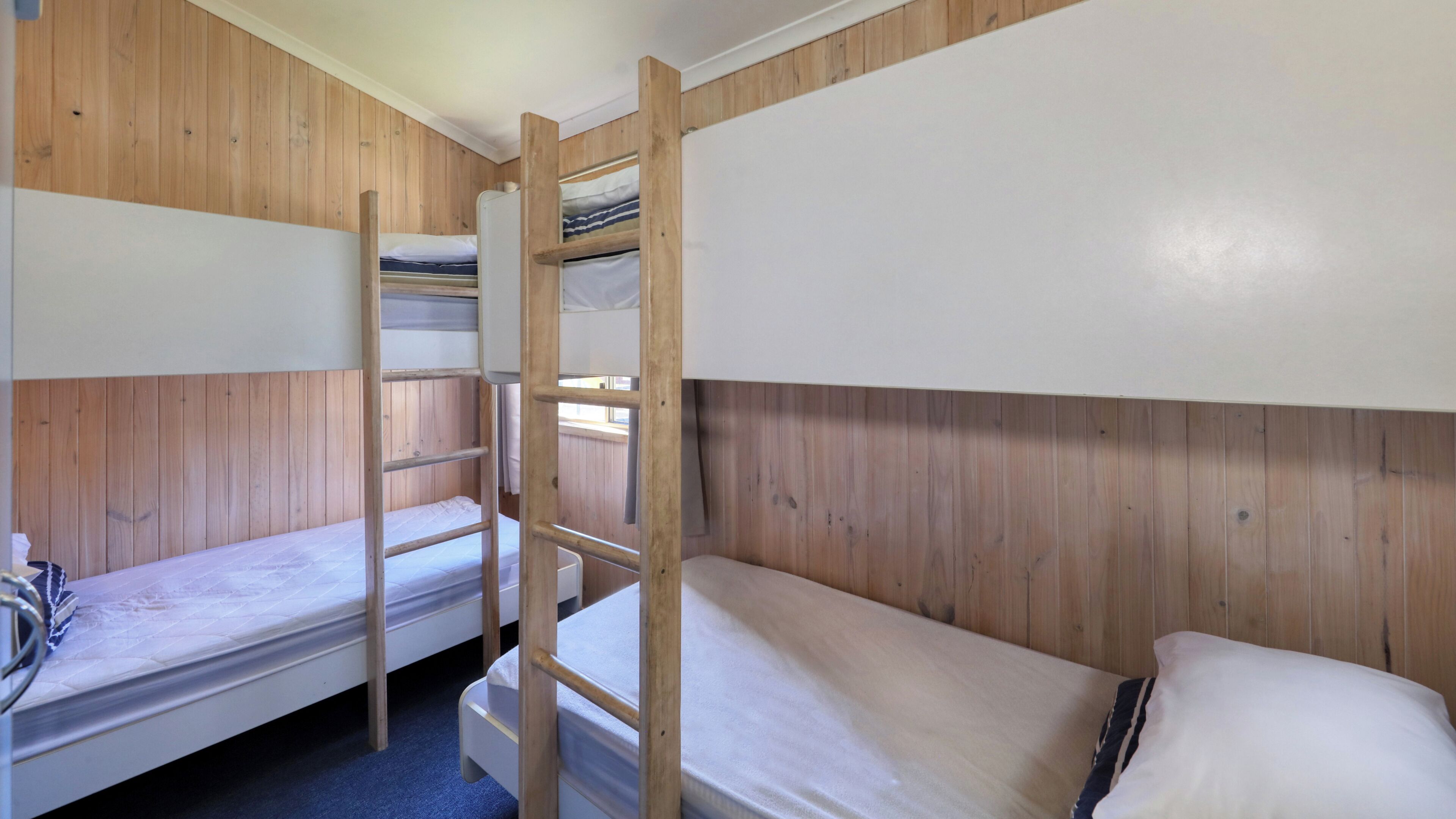 A bunk bed room with wooden walls, a ladder, and a single bed with a white mattress.