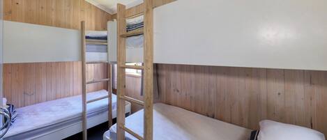 A bunk bed room with wooden walls, a ladder, and a single bed with a white mattress.
