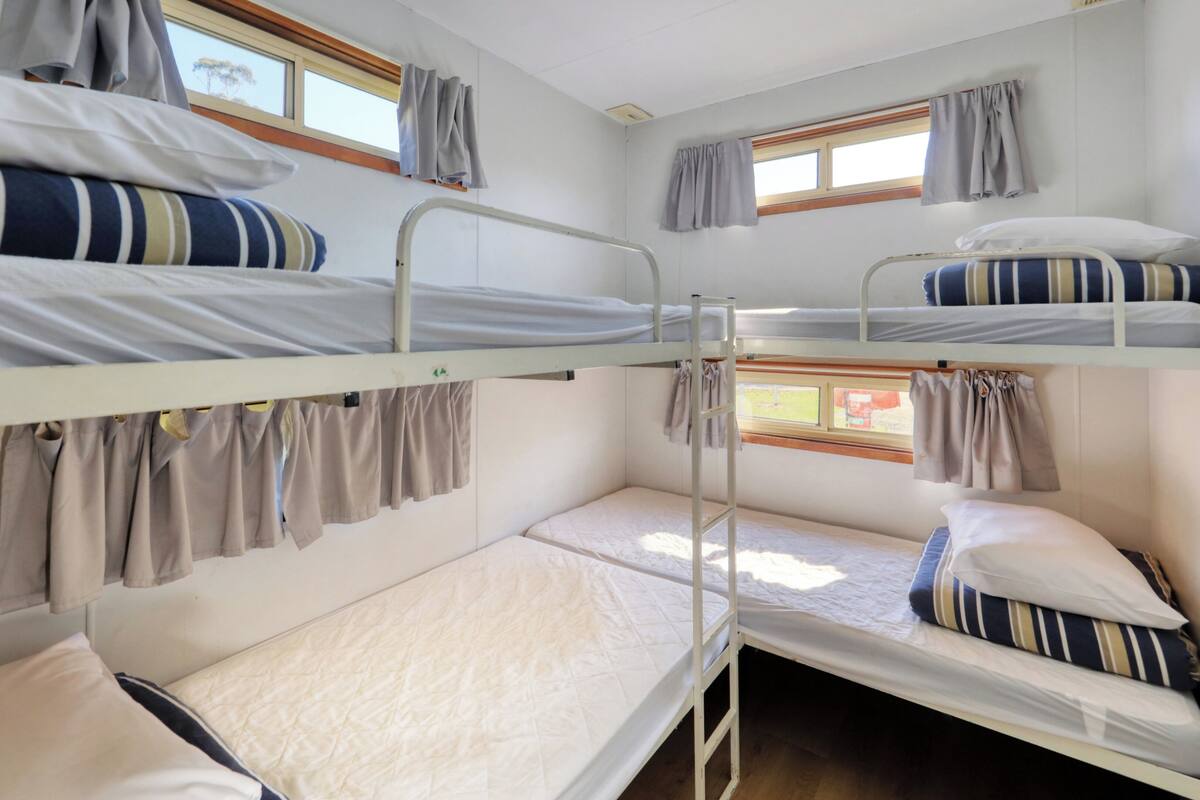 A bunk bed room with three levels, each with a mattress and pillows, and a window with curtains.