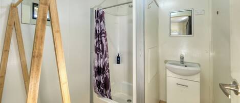 A bathroom with a shower, a sink, a mirror, and a wooden ladder.