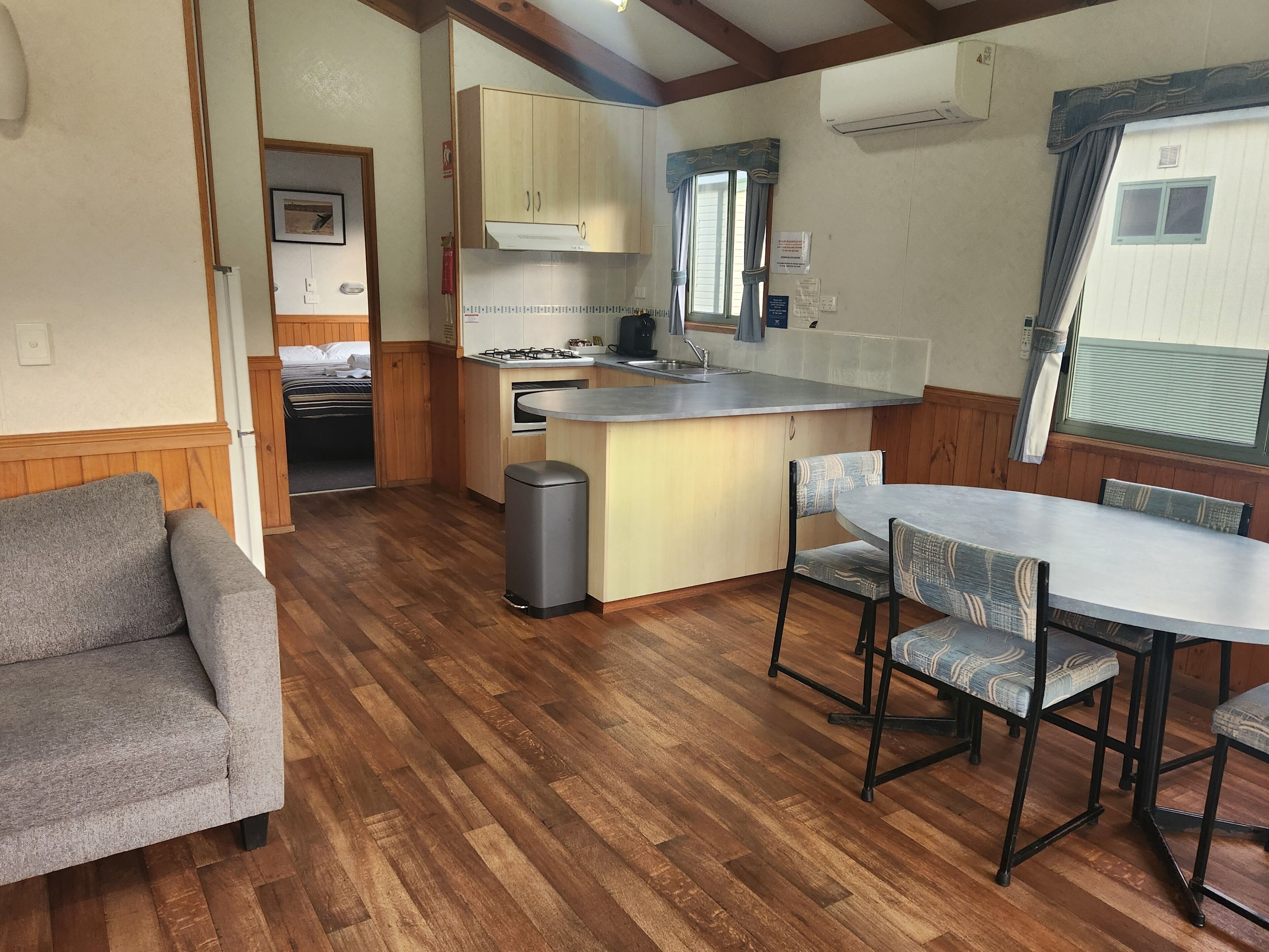 A compact kitchen with wooden cabinets, a sink, and a stove. There is a dining area with a table and chairs.
