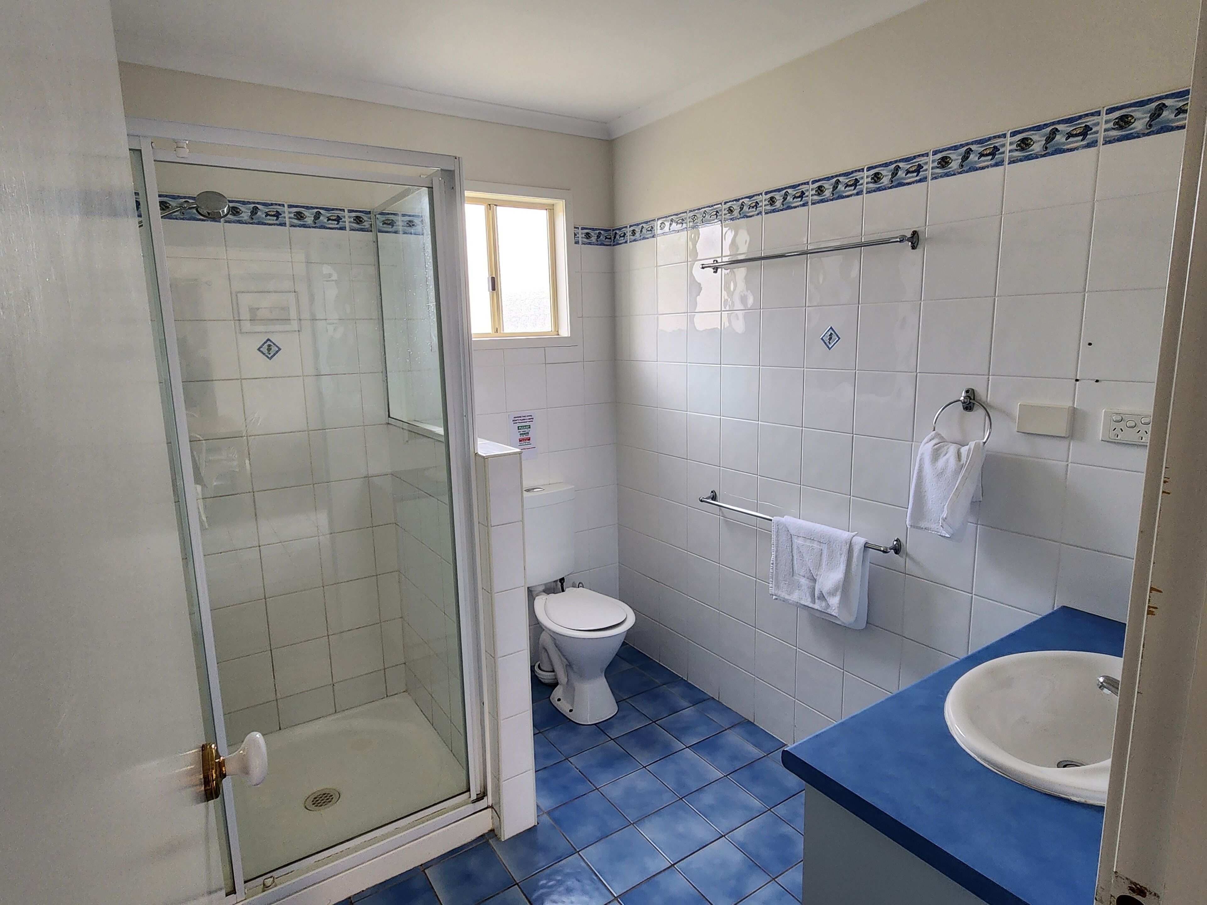 A bathroom with a glass shower enclosure, a toilet, a sink, and a towel rack.