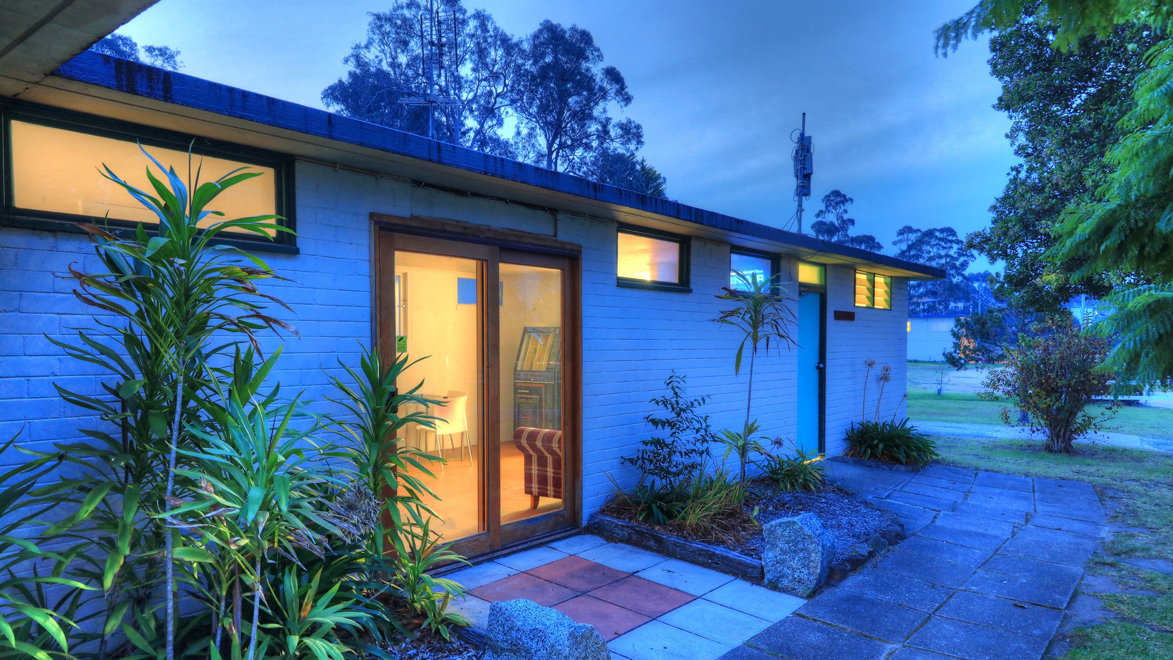 A modern house with a glass door, a small garden, and a paved driveway.