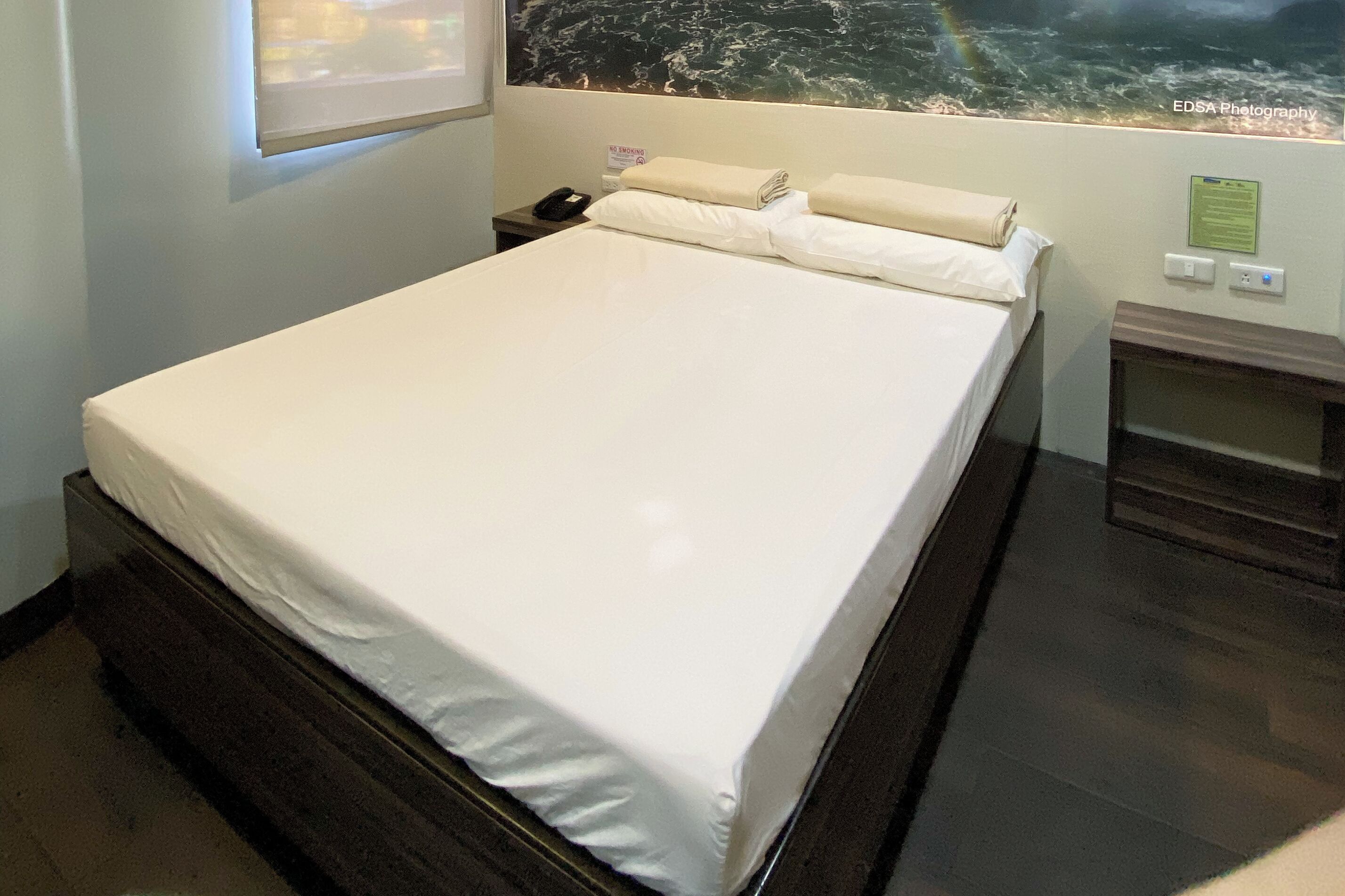 A neatly made bed with white linens, a bedside table with a phone, and a wall-mounted sign.