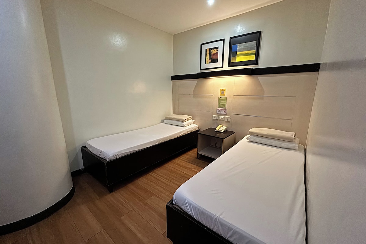 A hotel room with two single beds, a bedside table with a lamp, and a wall-mounted telephone.