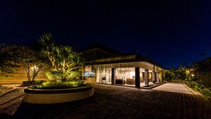 A modern building with a well-lit entrance, a paved driveway, and a landscaped garden area. - Luxotic Private Villa and Resort (Nusa Dua)