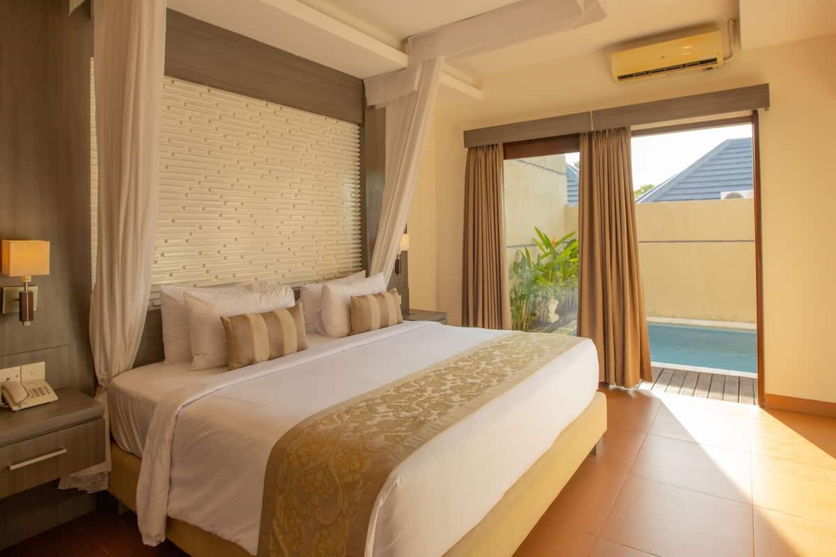 Une chambre spacieuse avec un grand lit, un mur d’accent en briques blanches, un téléphone sur la table de chevet et une vue sur une piscine.