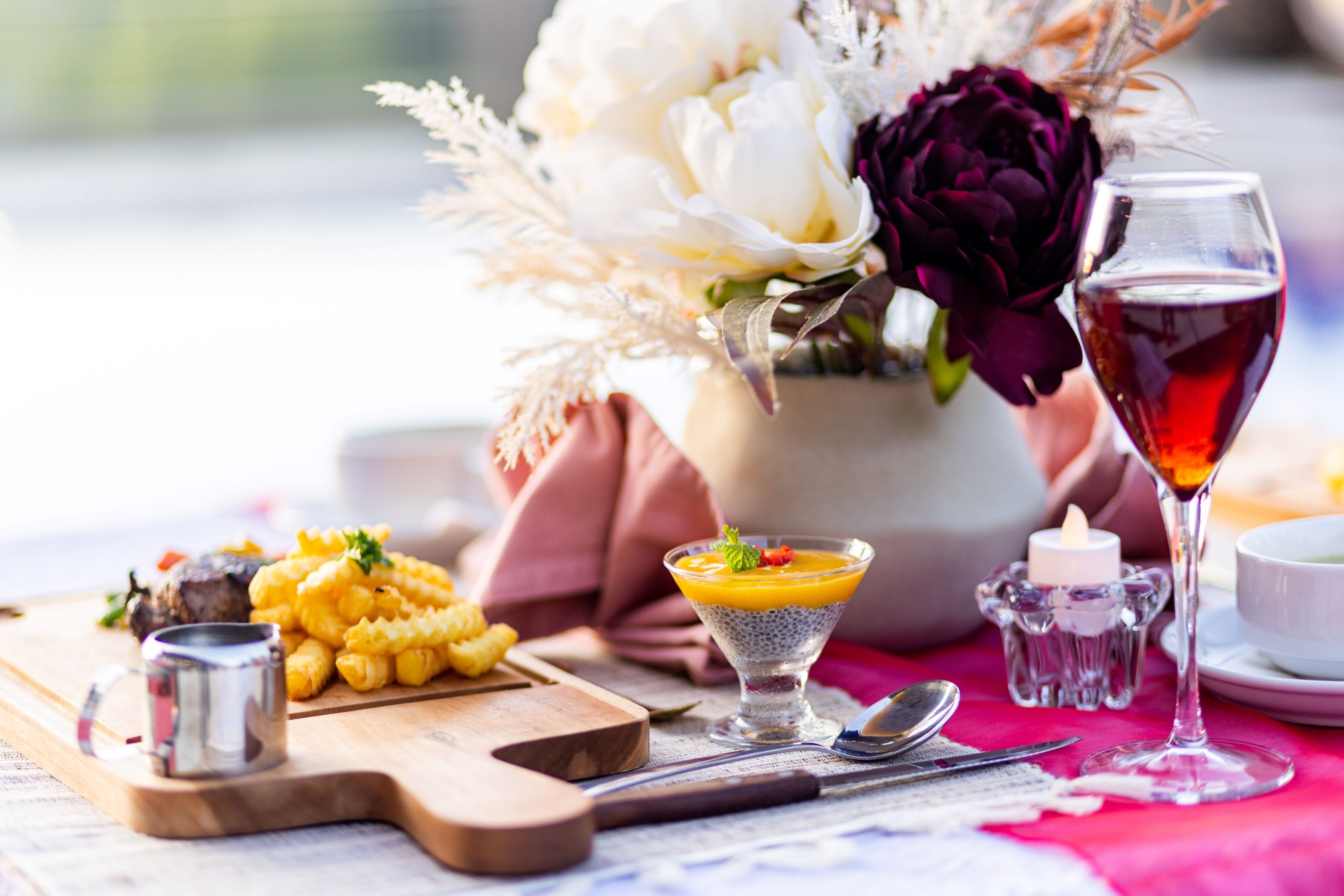 A dining table with a variety of dishes, a glass of red wine, and a vase with flowers.