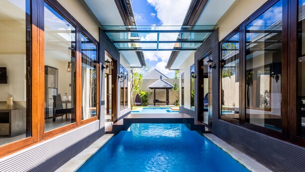 A modern swimming pool with glass walls and wooden accents, leading to a covered patio area. - Luxotic Private Villa and Resort (Nusa Dua)