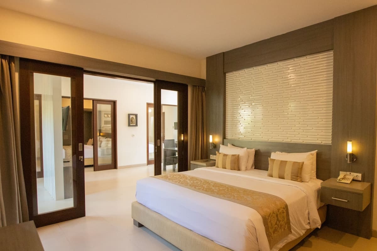 Une chambre d’hôtel avec un grand lit, une table de chevet, un téléphone et une fenêtre avec des stores.