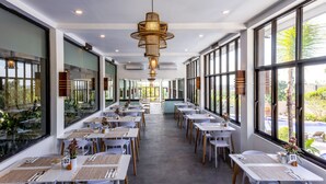 A spacious dining area with multiple tables and chairs, large windows, and a central hanging light fixture. - Luxotic Private Villa and Resort (Nusa Dua)