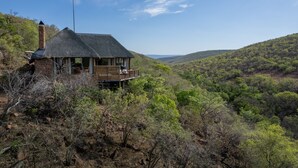 A thatched-roof house with a balcony, surrounded by a forested landscape.