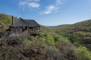 Une maison au toit de chaume, dotée d’un balcon, entourée d’un paysage boisé.