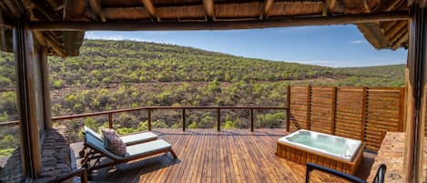 Eine Holzterrasse mit Liegestühlen und einem Whirlpool mit Blick auf eine Berglandschaft.
