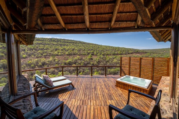 Une terrasse en bois avec des chaises longues et un jacuzzi, offrant une vue sur un paysage montagneux.