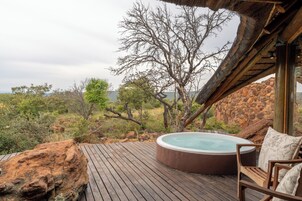 Un jacuzzi en una terraza de madera con vistas a un paisaje rocoso y árboles.