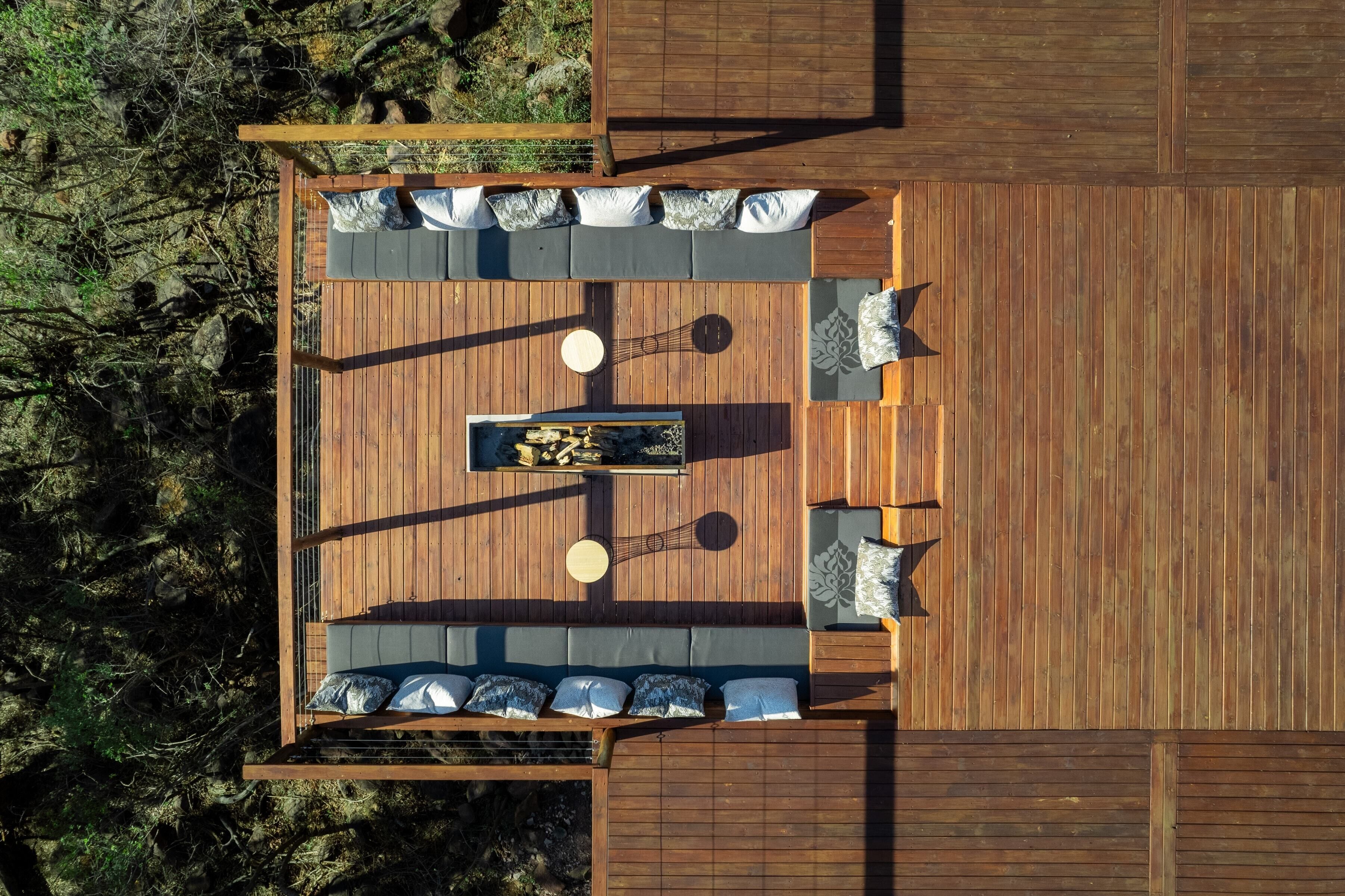 A wooden deck with a central seating area, surrounded by a wooden fence, and a view of the surrounding landscape.