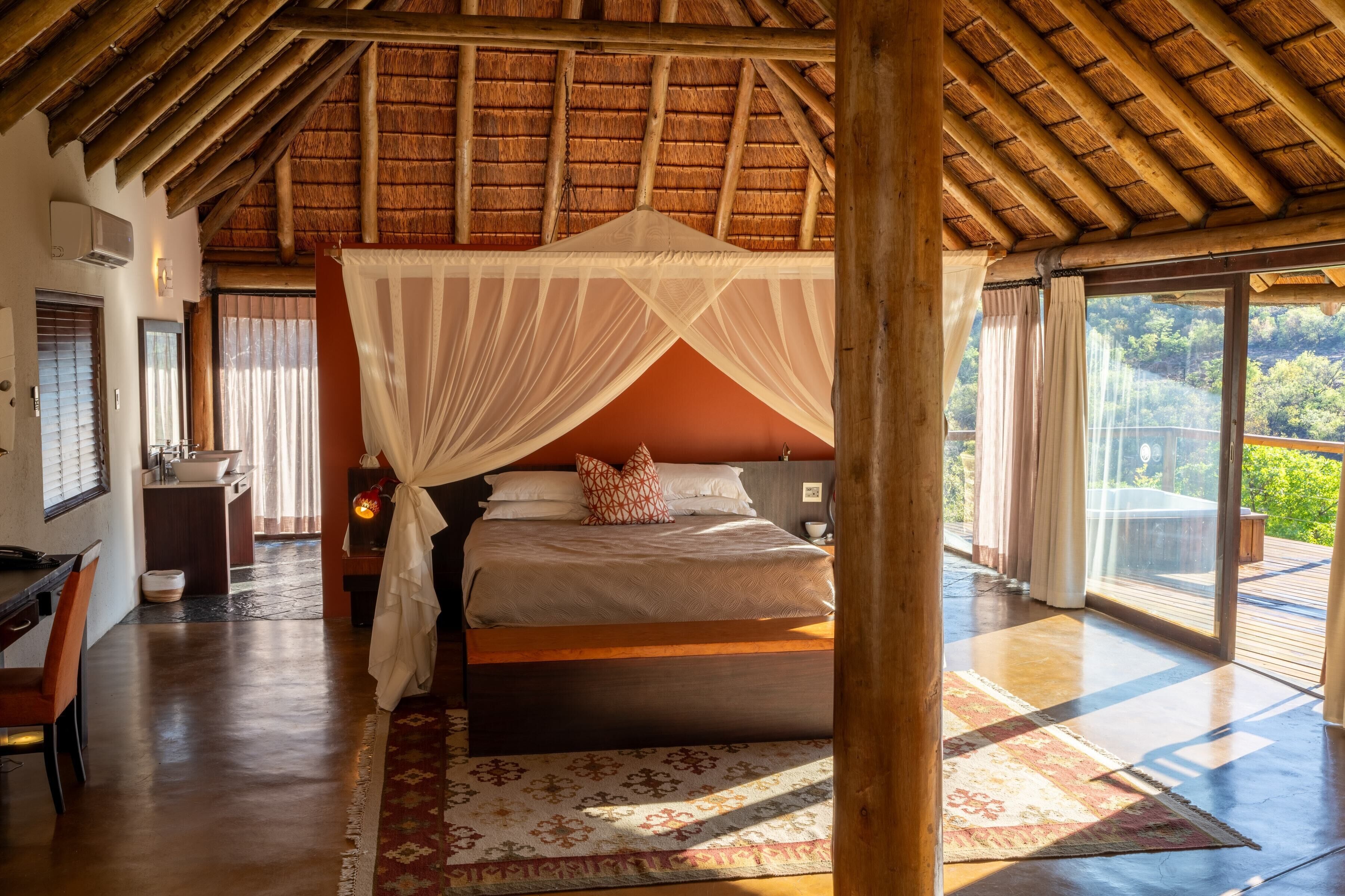 Quarto com cama de dossel, teto de madeira e vista para o exterior.
