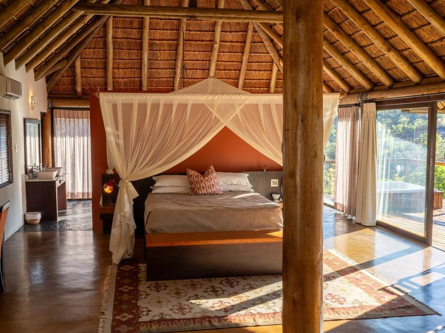 Quarto com cama de dossel, teto de madeira e vista para o exterior.