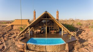 Un bâtiment à toit de chaume, doté d’une piscine, entouré d’un paysage rocheux.