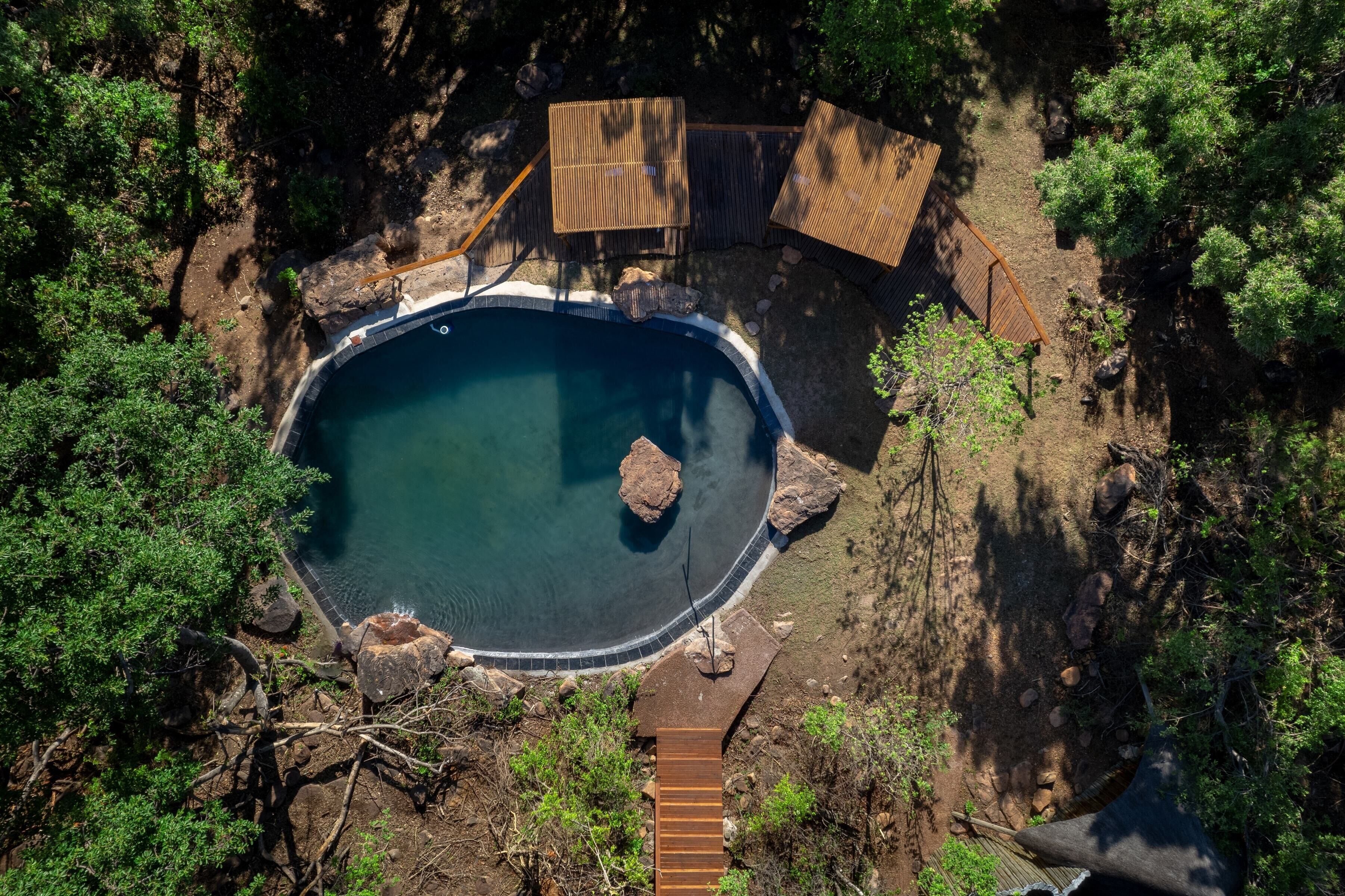 An aerial view of a swimming pool surrounded by natural vegetation and wooden structures.