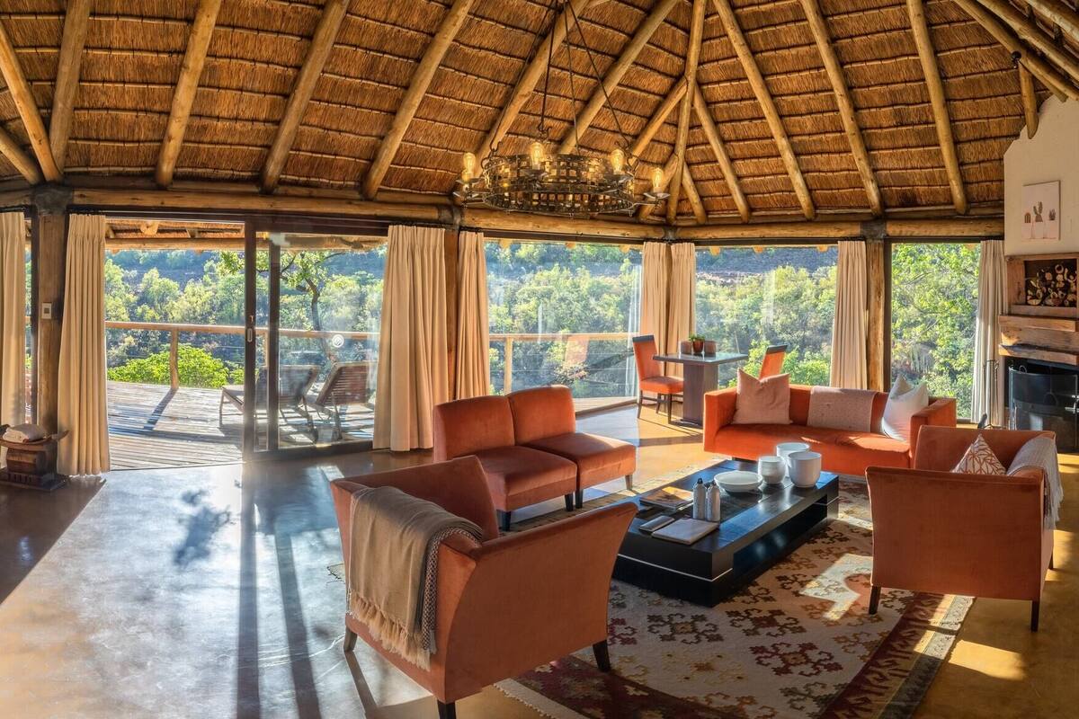 Ein geräumiges Zimmer mit hoher Decke, einem Bett, einer Sitzecke mit Sofas und großen Fenstern mit Blick ins Freie.