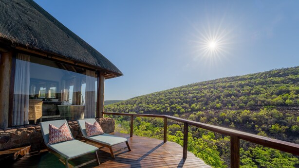 Une terrasse en bois avec deux chaises longues et une table, offrant une vue sur un paysage verdoyant et luxuriant.