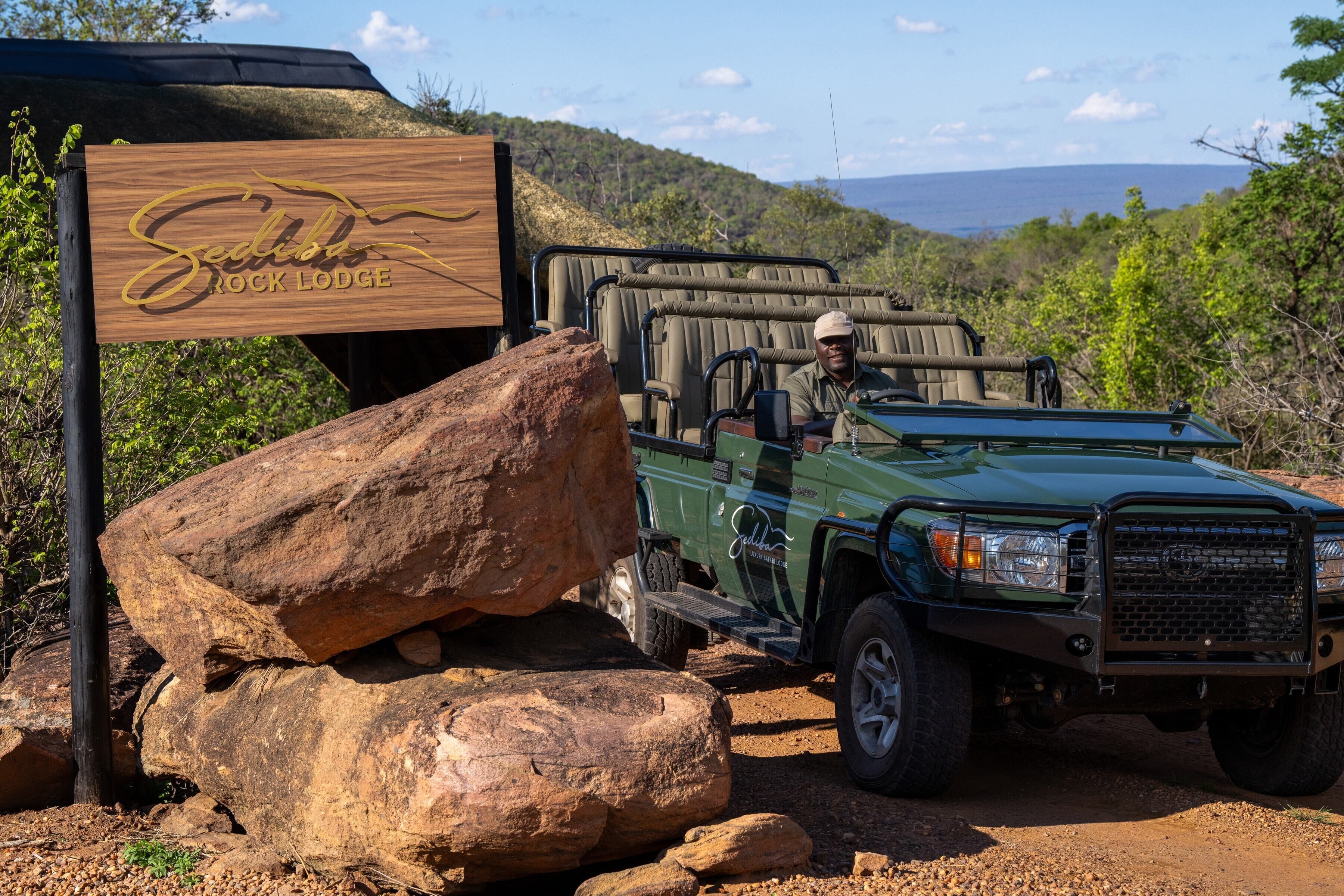 A green SUV parked at a campsite with a sign reading "Sedibah Rock Lodge".