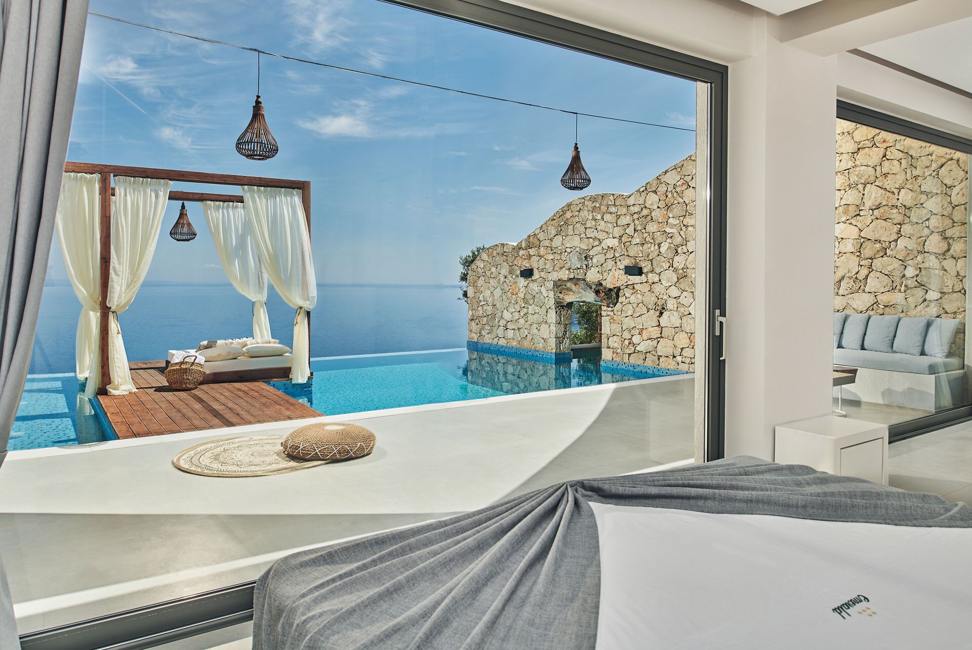 A modern bedroom with a large window overlooking a private infinity pool and the sea.