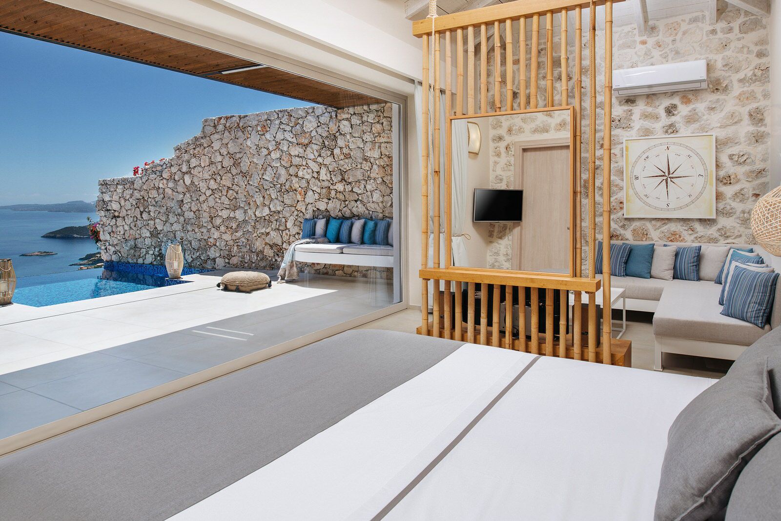 Un dormitorio moderno con pared de piedra, un ventanal con vistas al mar, una cama, un televisor y un panel de madera.