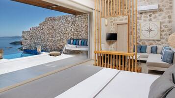 Un dormitorio moderno con pared de piedra, un ventanal con vistas al mar, una cama, un televisor y un panel de madera.