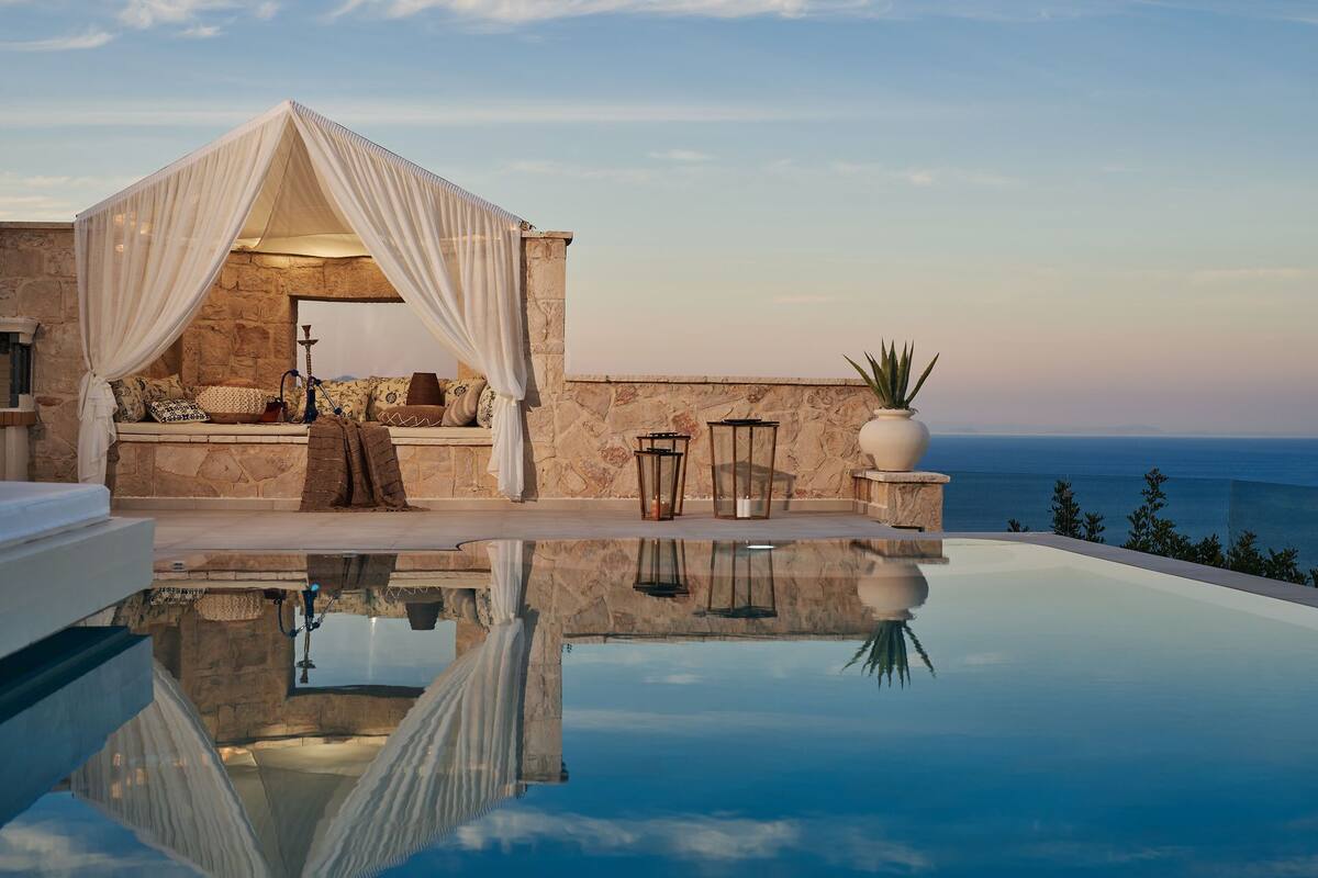 Un espace extérieur luxueux, aménagé avec un mur en pierre en arrière-plan, offrant une vue dégagée sur la mer et comprenant un bassin dont la surface reflète la lumière.