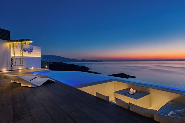 Terraza moderna en la azotea con piscina, zona de estar y vistas al océano al atardecer.