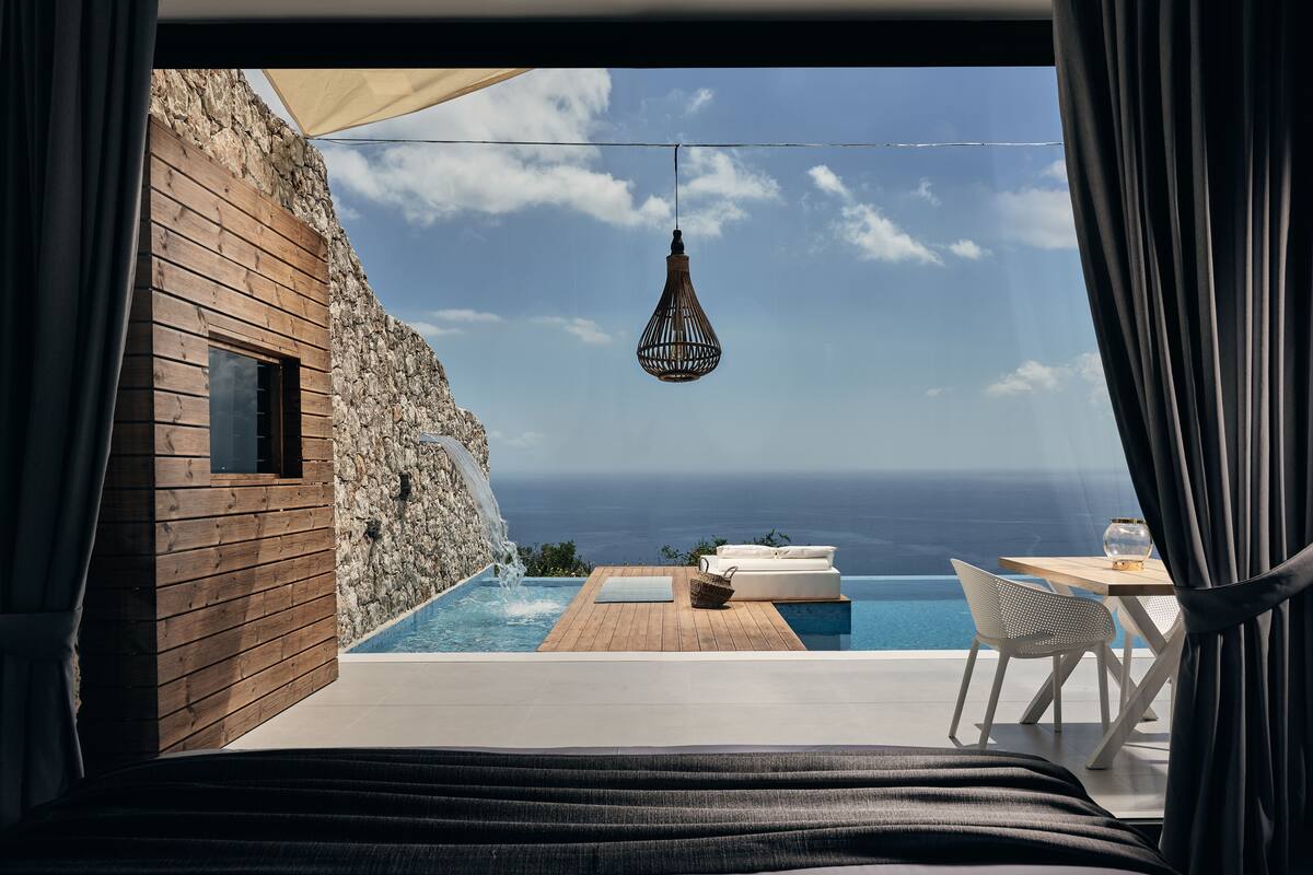Une chambre avec vue sur l’océan, un mur en bois, un luminaire suspendu, une petite piscine et une table avec une chaise.