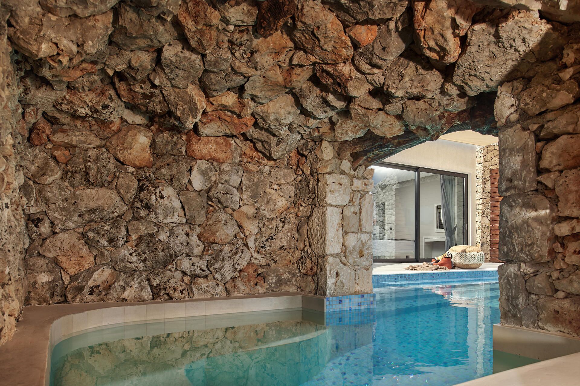 A stone-walled indoor pool area with a clear view into a modern bathroom.