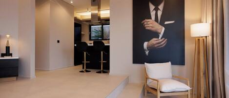 Een moderne hotellobby met een minimalistisch design, met een groot portret, een zithoek en een trap naar een andere ruimte.