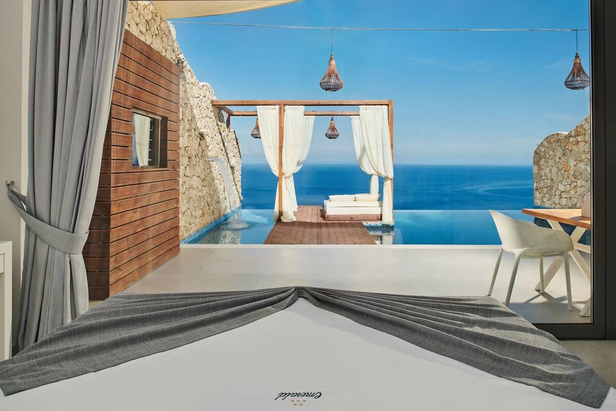 Une chambre avec vue sur la mer, un mur en bois, un lit et un petit coin salon avec une table et une chaise.