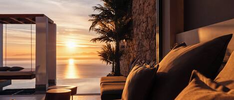 Quarto moderno com vista para o pôr do sol sobre o oceano, uma palmeira e um lustre.