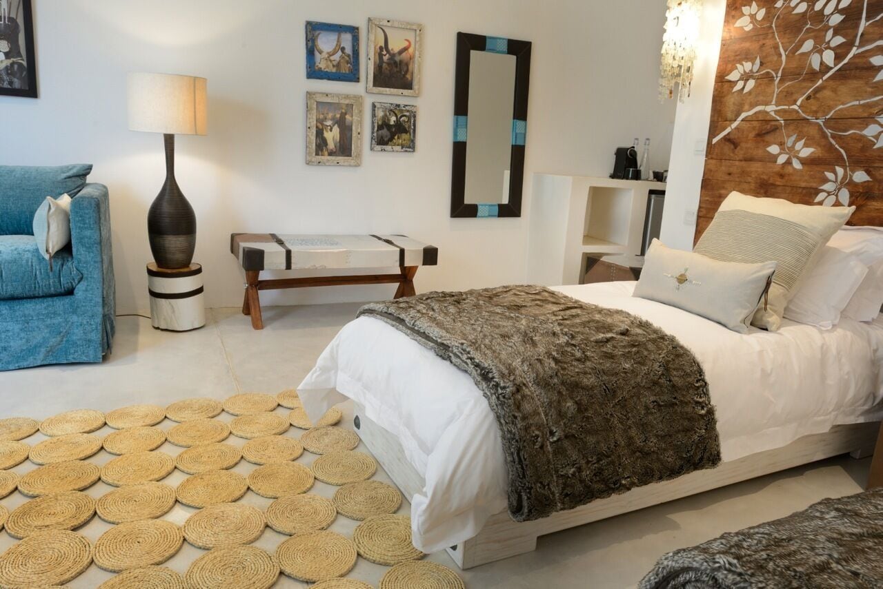 A bedroom with a bed, a blue sofa, a bedside table with a lamp, and wall art.