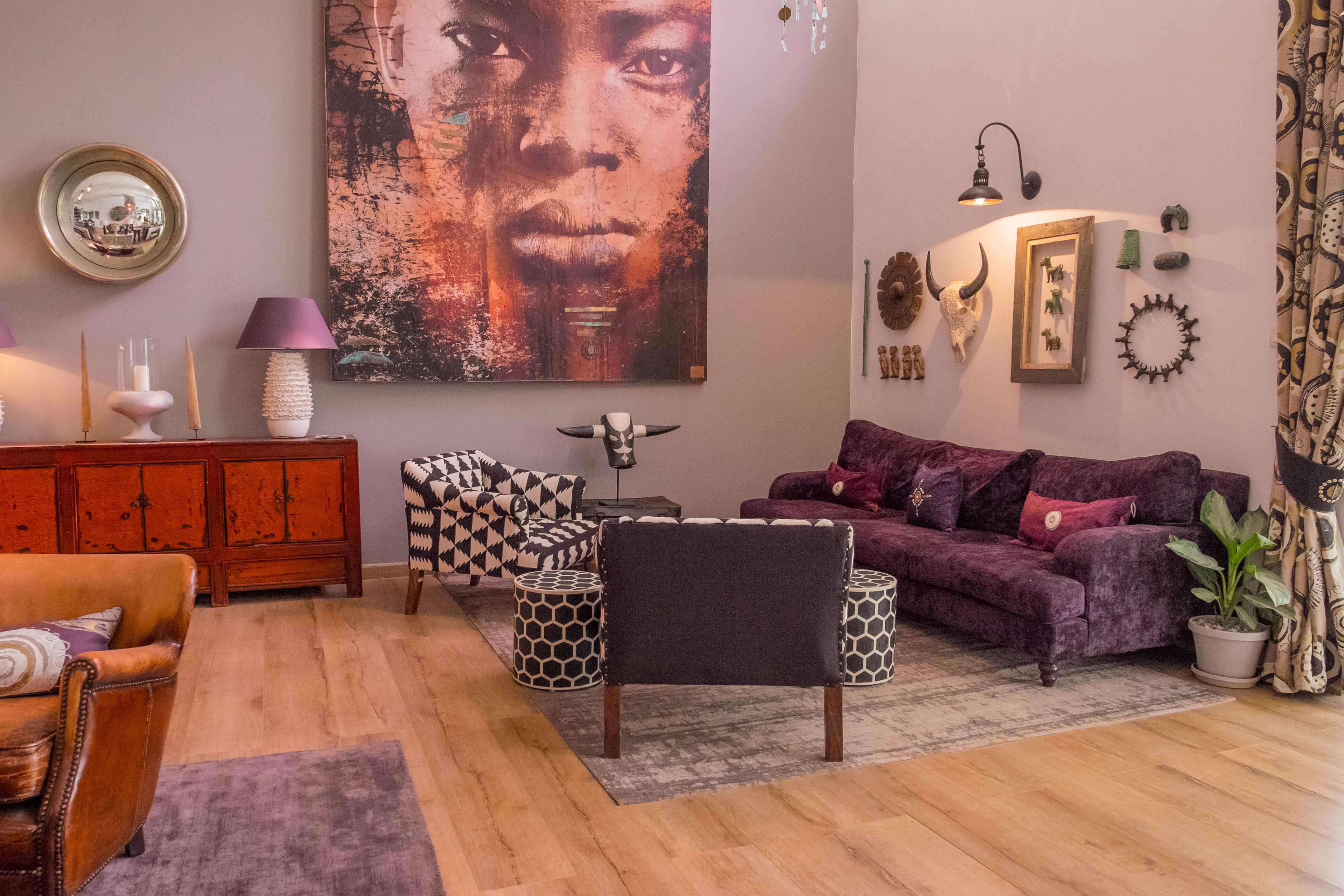 A living room with a sofa, armchair, and ottoman, a wooden cabinet, and a large abstract painting.