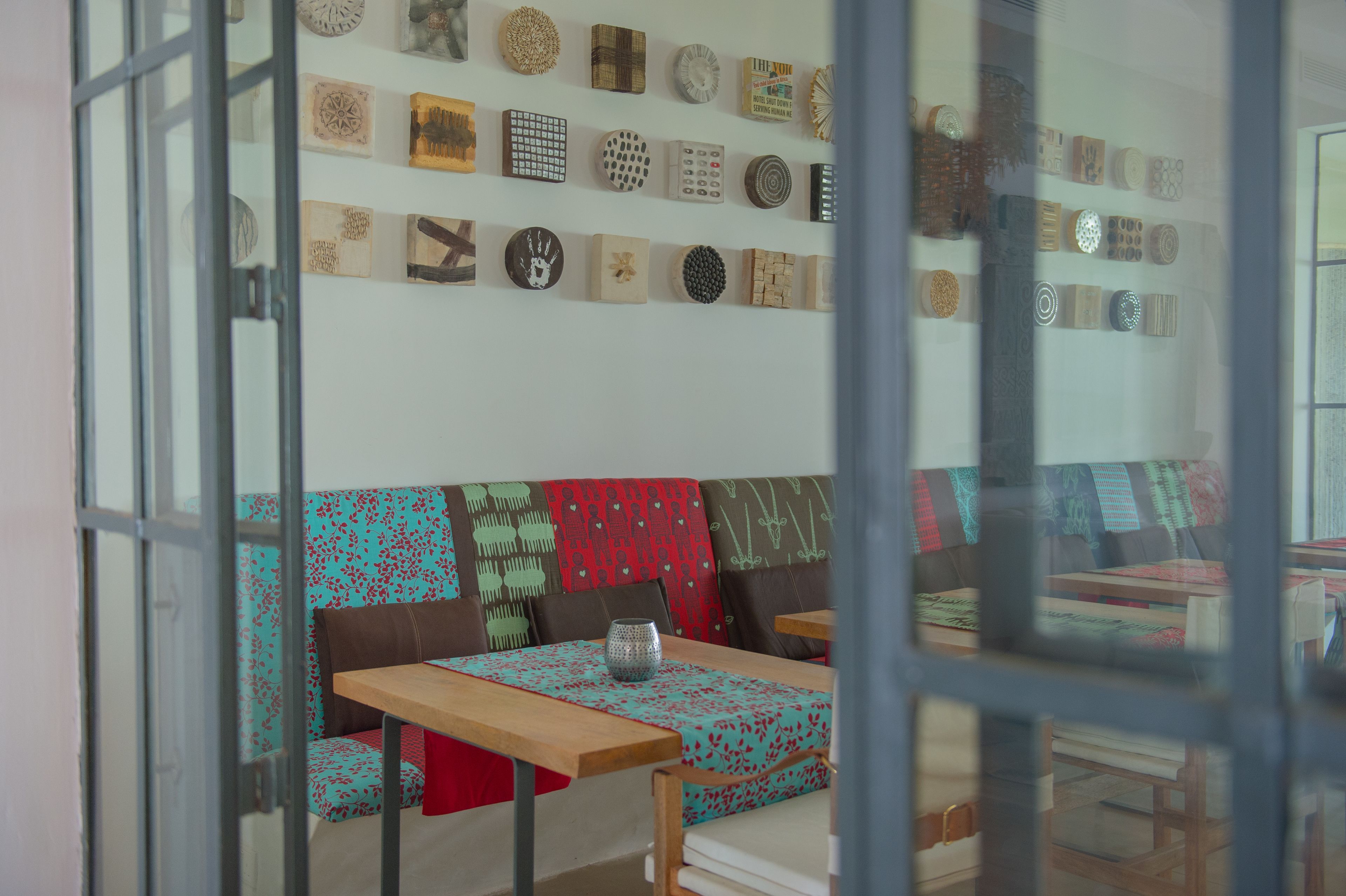 Un comedor con una mesa y bancos de madera, una pared con varios platos decorativos, y vista a través de un ventanal.