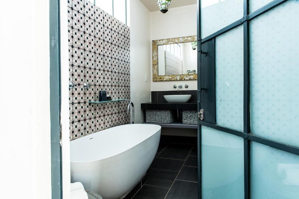 Une salle de bain moderne avec une baignoire sur pieds, un grand miroir et un mur recouvert de carreaux formant un motif géométrique.