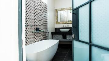 A modern bathroom with a freestanding bathtub, a large mirror, and a tiled wall with a geometric pattern.