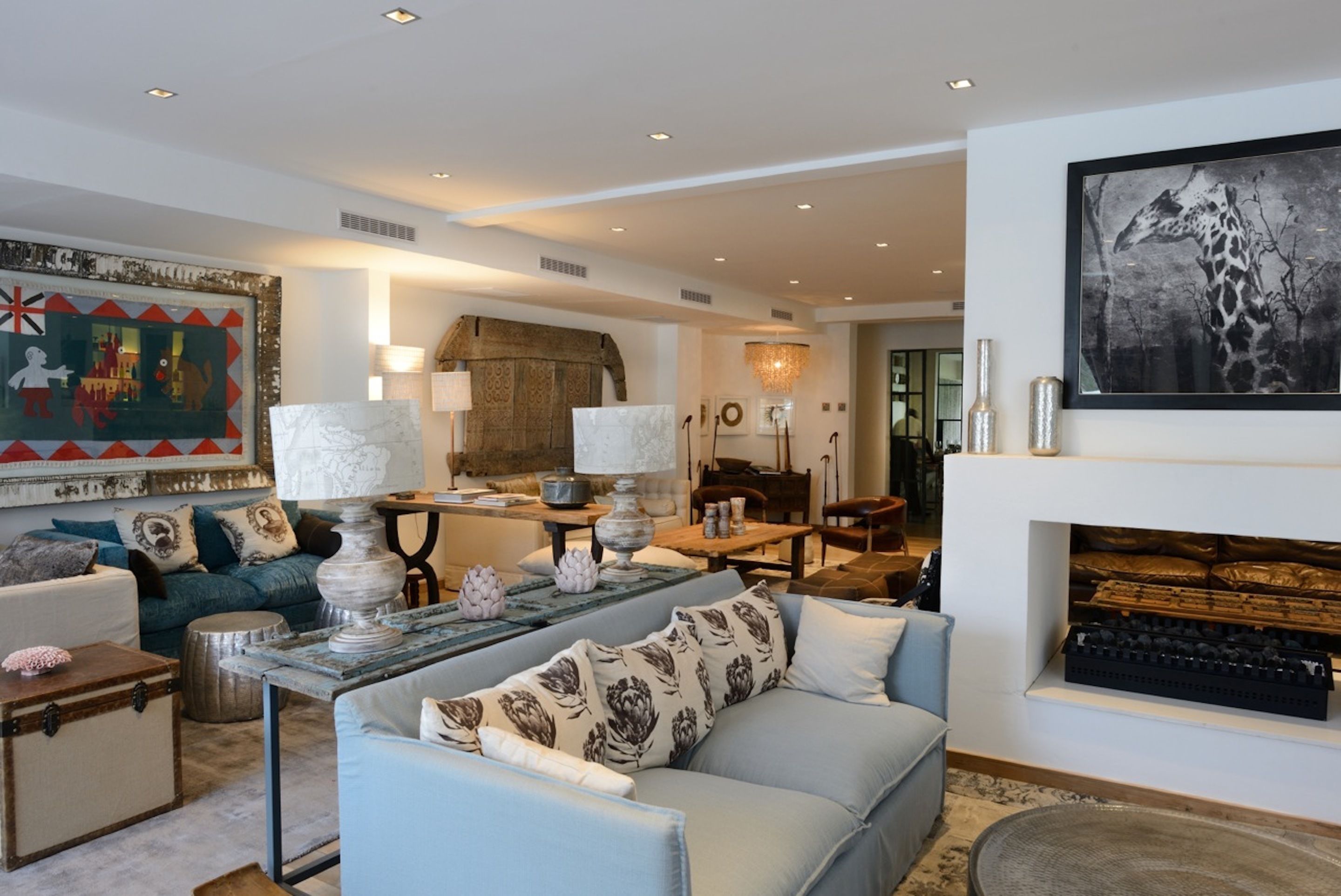A modern living room with a sofa, a coffee table, and a fireplace. There is a painting on the wall and a chandelier.