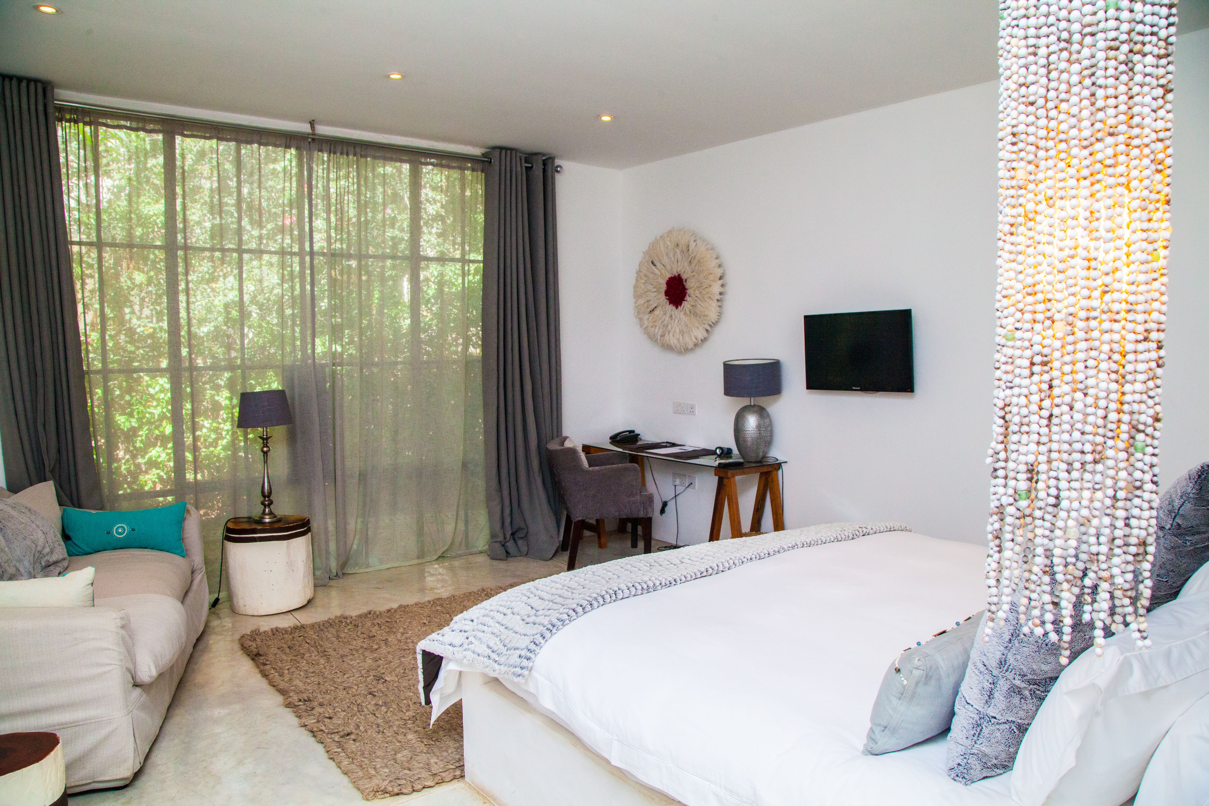 A bedroom with a large bed, a desk, a chair, a TV, and a window with curtains.