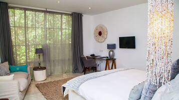A bedroom with a large bed, a desk, a chair, a TV, and a window with curtains.