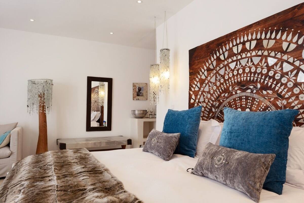A modern bedroom with a large bed, blue and grey pillows, a wooden headboard with a decorative panel, and a hanging light fixture.