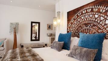A modern bedroom with a large bed, blue and grey pillows, a wooden headboard with a decorative panel, and a hanging light fixture.
