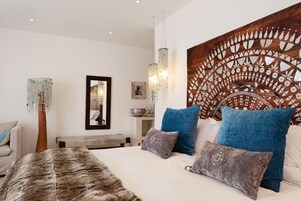 A modern bedroom with a large bed, blue and grey pillows, a wooden headboard with a decorative panel, and a hanging light fixture.