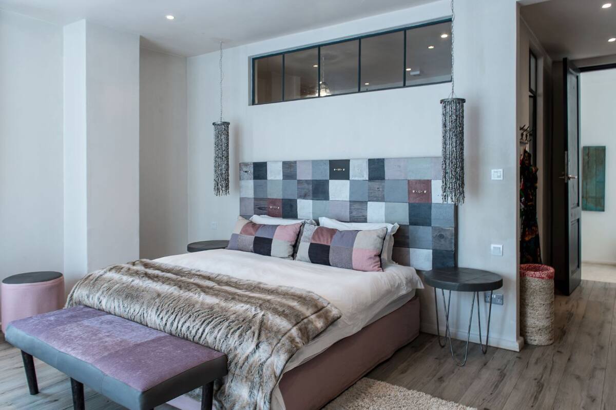 A modern bedroom with a large bed, a bench, two side tables, and a unique checkered headboard.
